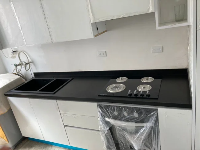 Cocina con encimera negra y mobiliario blanco durante la instalación