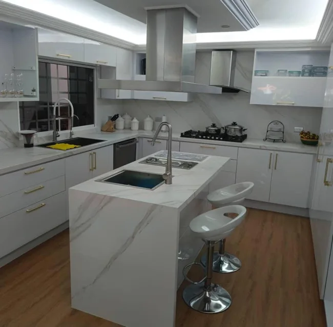 Cocina blanca con isla, campana y asientos en la barra